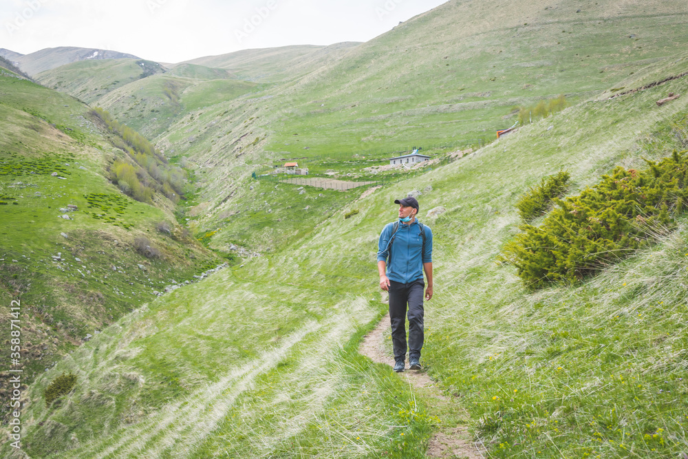 Male person with face mask on is walking down the path in nature. Post pandemic travel and self isolation around nature. Solo adventure in Kazbegi national park. Georgia