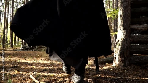 Man playing larp is wearing black cloak and walking through the forest. The actor is holding the stick and moves forward in the woods. The conception of live acting role plays and actors. photo