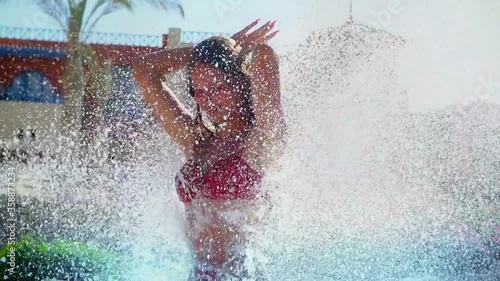 Slow motion of palm tree summer season for girl model posing relax in swimming pool with water fountain under waterfalls splashing water and sun sparks . Large drops water fall on young woman hand up.