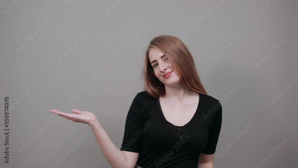 Palms up, place your product here, raising arms wide spread is catching something. Young attractive woman, dressed black t-shirt, grey background Palms up, place your product here, raising arms wide spread is catching something. Young attractive woman, dressed black t-shirt, grey background