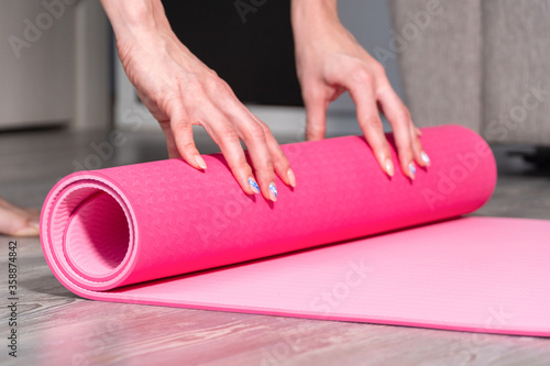 Close-up of attractive young woman folding yoga or fitness mat after working out at home in living room.