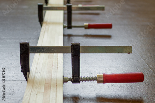 Close up of the process of cutting wooden slats fixed with clamps lying on the dark floor of cork. Repair concept photo