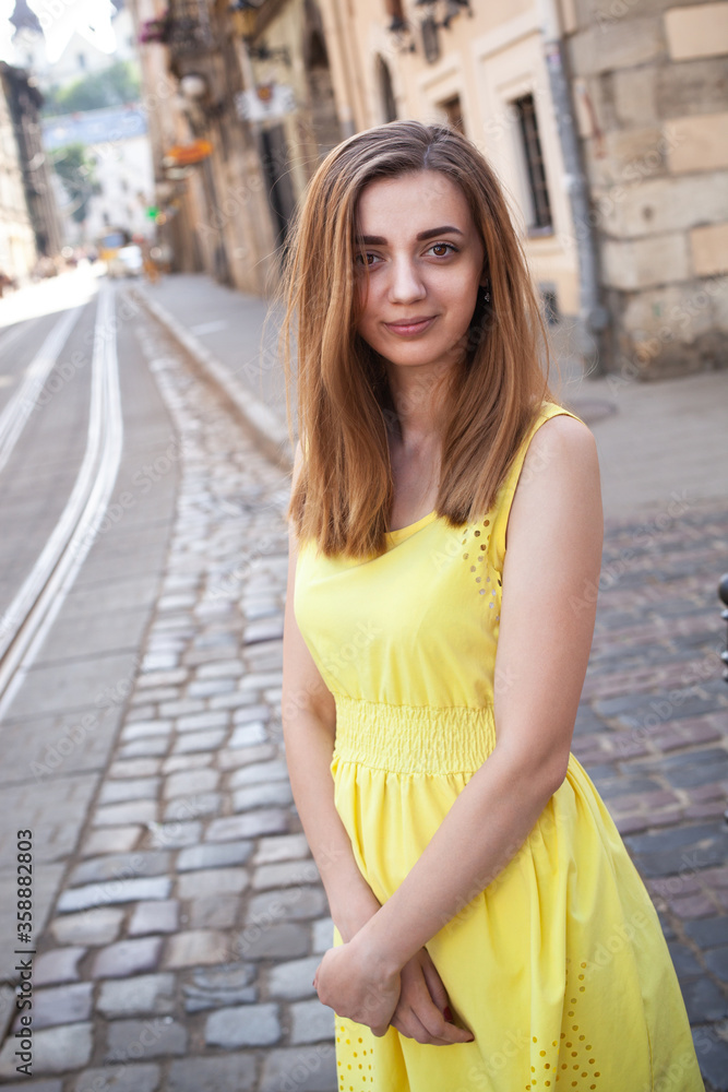Fototapeta premium Pretty long hair brunette girl in yellow light dress walking outdoor