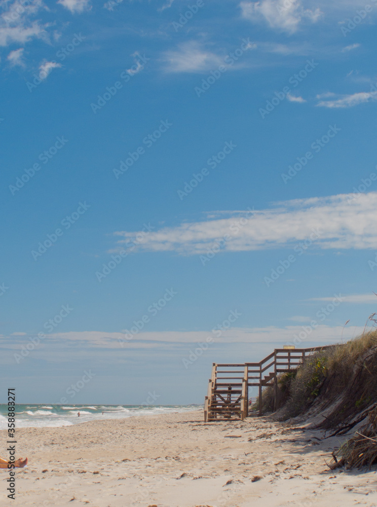 Stairs on a beach in central Florida with sunbather and people swimming. Serene beach scene with blue sky, sand and waves