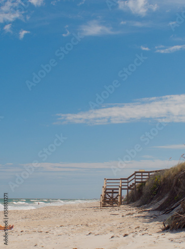 Stairs on a beach in central Florida with sunbather and people swimming. Serene beach scene with blue sky  sand and waves