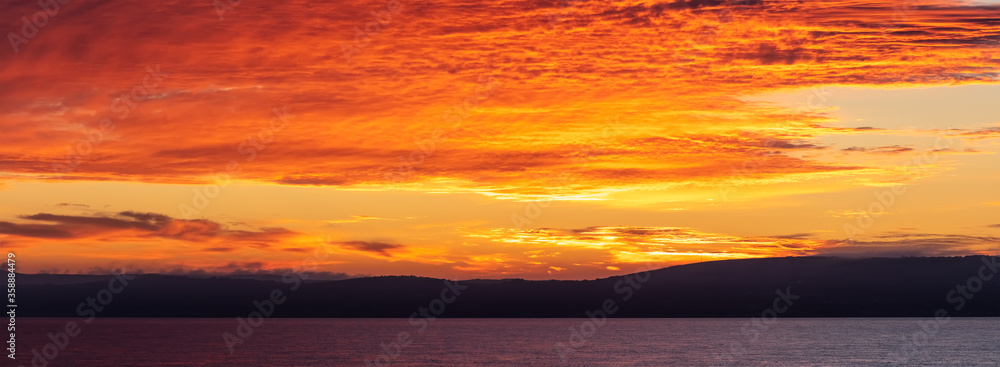 Amazing panorama. Scenic red-and-orange sunset with a shoreline as a silhouette in the foreground.
