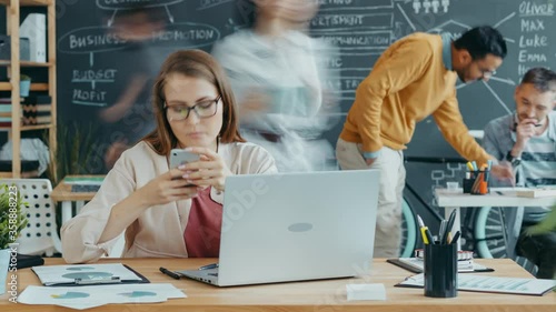 Time lapse of business lady busy with work in open space office cooperating with colleagues, people are moving around quickly while woman is sitting at desk.