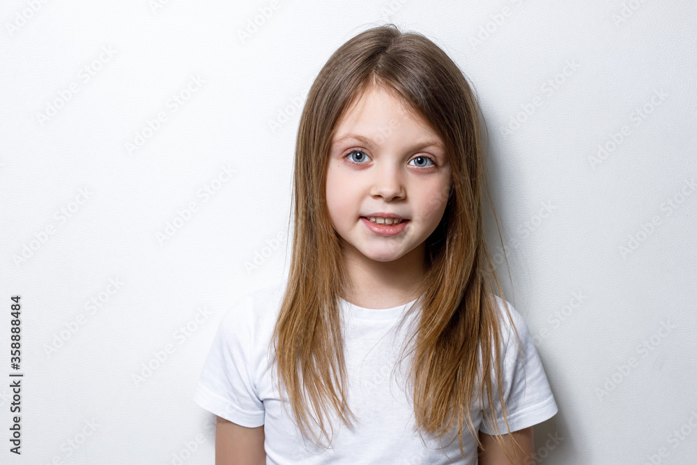 A beautiful healthy little girl in white clothes on a white background smiles and looks at the camera. Copy space for text A beautiful healthy little girl in white clothes on a white background smiles and looks at the camera. Copy space for text