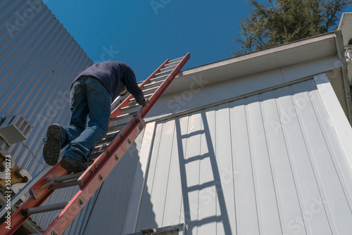Riesgos de un trabajador en una escalera durante trabajo en el techo de una casa en un hermoso día soleado. photo