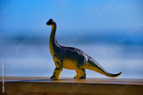 Dinosaur toy standing outside with the beach and ocean in the background.