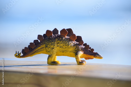 Dinosaur toy standing outside with the beach and ocean in the background. © CarlyZel