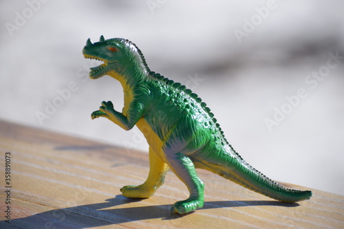 Dinosaur toy standing outside with the beach and ocean in the background.