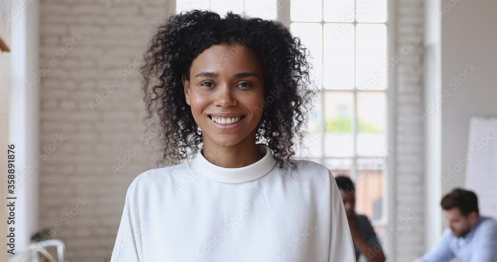 Smiling young african american female leader office worker intern standing in modern office looking at camera, happy mixed race employee business coach millennial professional hr close up portrait Smiling young african american female leader office worker intern standing in modern office looking at camera, happy mixed race employee business coach millennial professional hr close up portrait