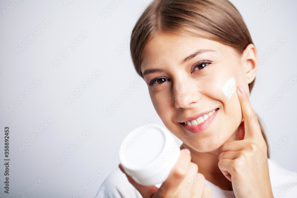 Young woman with beautiful skin puts moisturizing cream on her face