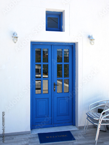 A blue entrance door in a white wall on a street in the traditional village of Megalochori in Santorini, Greece.