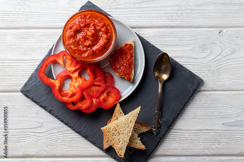 Ajvar or pindjur red vegetable sauce, paprika pepper on a black board and wooden table. Serbian traditional food. Horizontal orientation photo