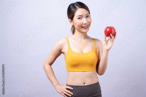 A sporty Asian woman in sportswear holding an apple isolated on white background. Concept of healthy lifestyle