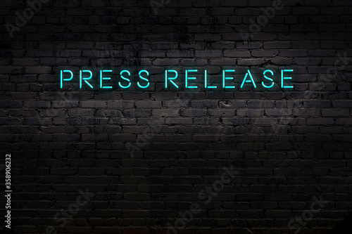 Night view of neon sign on brick wall with inscription press release