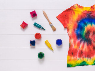 Brushes, paint, and a tie dye t-shirt on white boards. Flat lay.