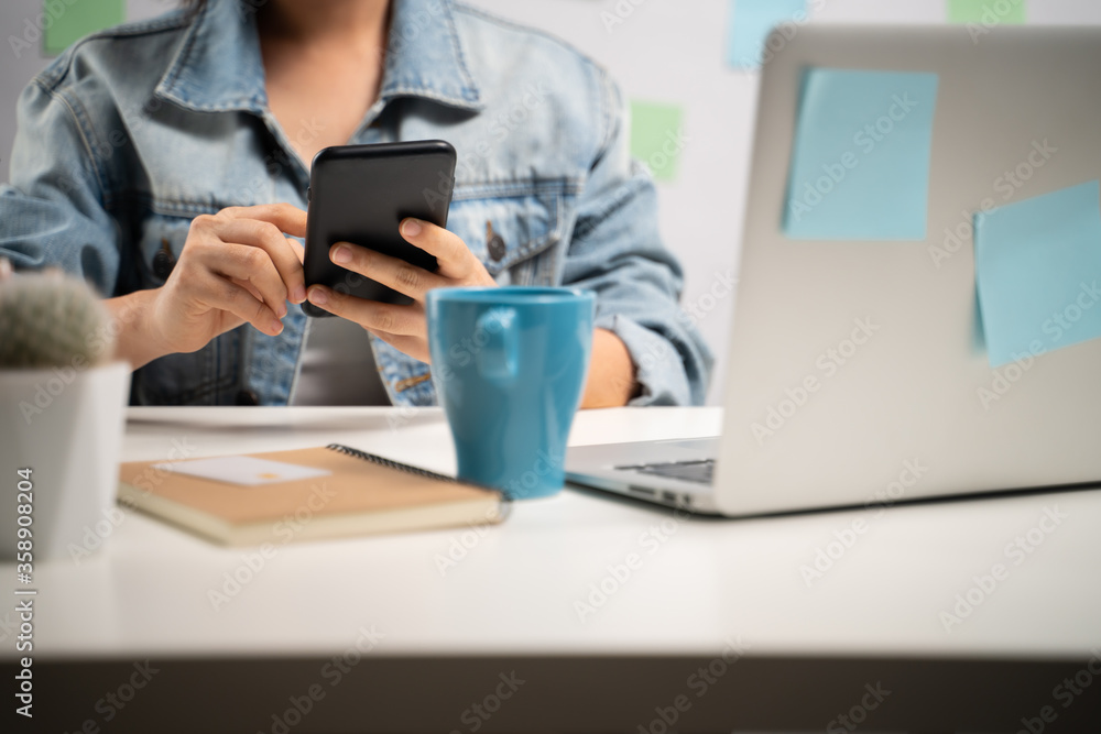 Asian woman happy smiling looking at smart phone and reading news at home office. WFH. Work from home. Prevention Coronavirus COVID-19 concept. Asian woman happy smiling looking at smart phone and reading news at home office. WFH. Work from home. Prevention Coronavirus COVID-19 concept.