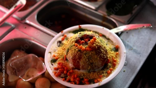 Making indian style street chaat and raj kachori with topped spices, red sauce and corns. 