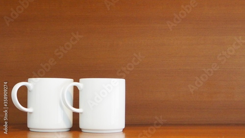Two stacking white porcelain mugs on wooden shelf in the kitchen room at home Living and lifestyle concept