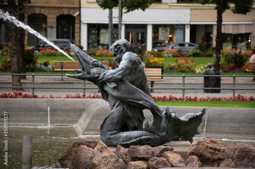 Art mermaid man and waterspout fish statue of water fountain in Mannheimer Wasserturm Water tower gardens in Friedrichsplatz square at Mannheim city on September 9, 2019 in Baden-Wurttemberg, Germany photo