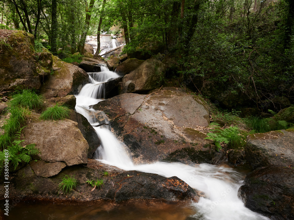 Obraz premium River Leça Waterfalls in Monte Cordova, Portugal. The river water runs down the big rocks of the mountain, under the green canopy of the trees in the spring
