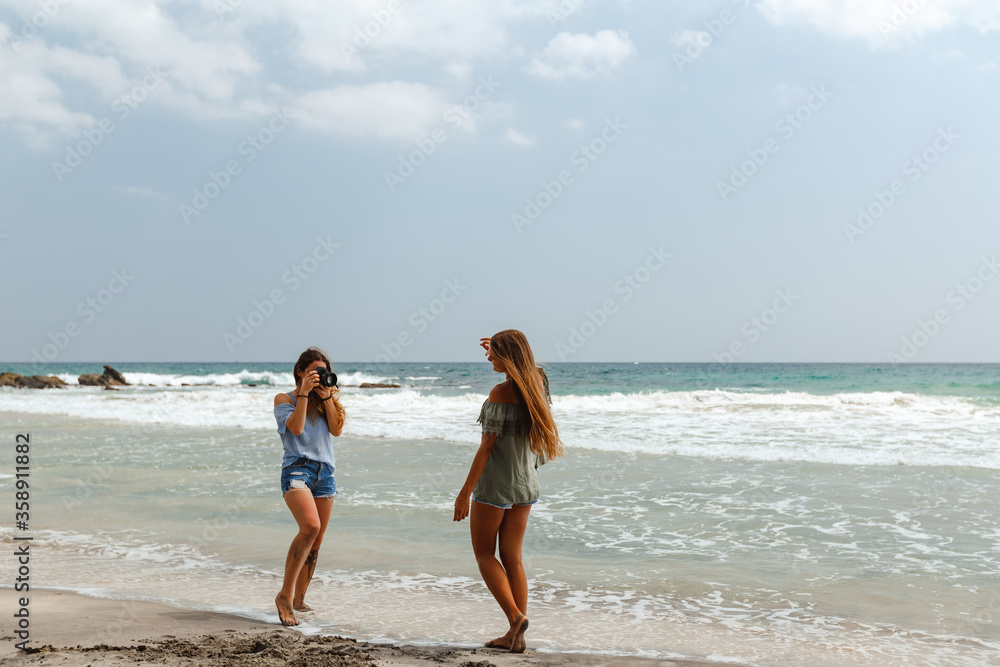 Traveling and photography. Young woman with camera a taking picture of her friend on the sea beach