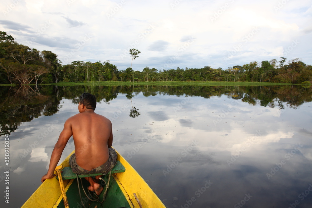 Shirtless man with paddle sitting on a fishing boat at sunset in Amazon jungle river, Brazil

