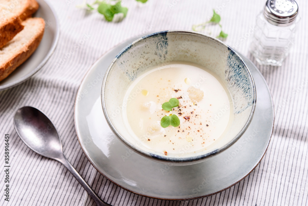 Cauliflower and Potato Cream Soup served with herbs and pepper on white linen striped tablecloth. Selective focus Cauliflower and Potato Cream Soup served with herbs and pepper on white linen striped tablecloth. Selective focus