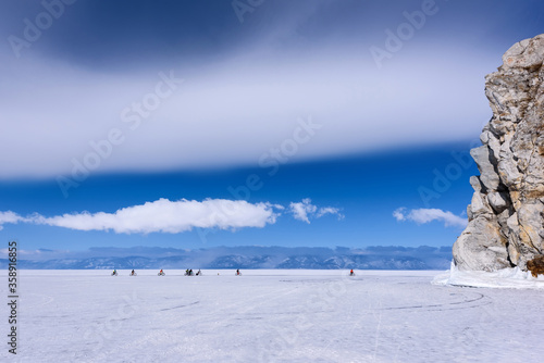 Group of people rides bicycle on the frozen lake Baikal near Cape Burkhan in sunny weather with beautiful clouds sky
