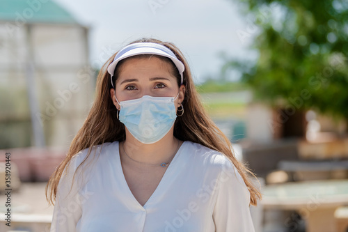 a young woman wearing a sport visor and a surgical mask outdoor . New lifestyle and safety concept.