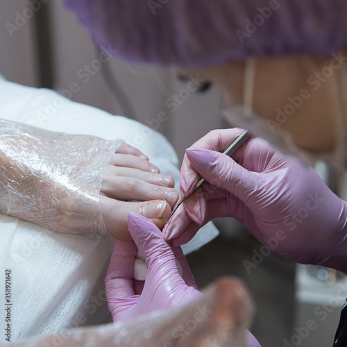 A pedicurist is processing toenails. The hands in the pink gloves. Salon pedicure. Pedicurist using pusher.