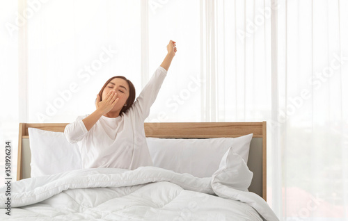 Portrait of young beautiful asian girl relax in white bedroom. Young Asian women in bed and waking up in the morning. Girl wakeup early morning feeling lazy and stretching her body on bed.