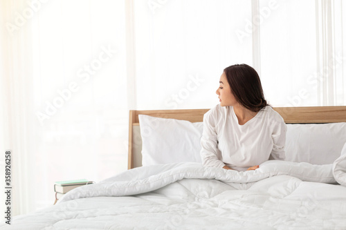 Young girl stretching in bed after wake up. Portrait of beautiful asian woman enjoying fresh soft bed linen mattress in bedroom. Woman Stretching in Her Bed. A Girl waking up in the Morning on bed.