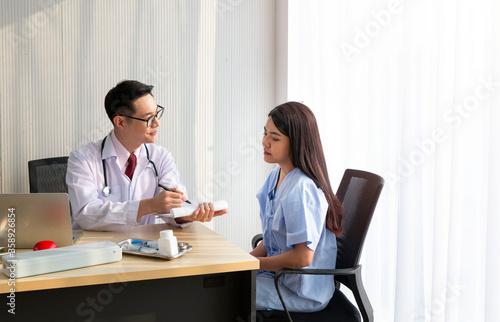 Doctor with female patient. Doctor and patient discussing something while sitting at the table, explaining diagnosis to his female patient. Medicine and healthcare concept. Coronavirus, Covid-19. © Avirut S.