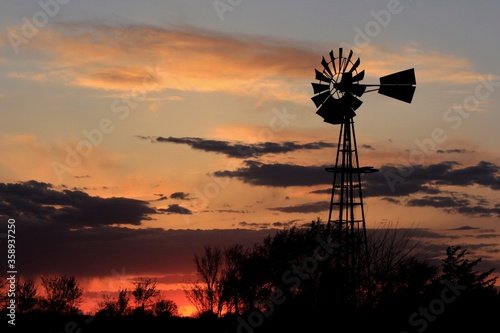 Kansas Country Windmill at Sunset with clouds and tree's north of Hutchinson Kansas USA.