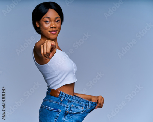 Happy woman in white top in oversize jeans smiles and shows victory gesture. Diet concept photo