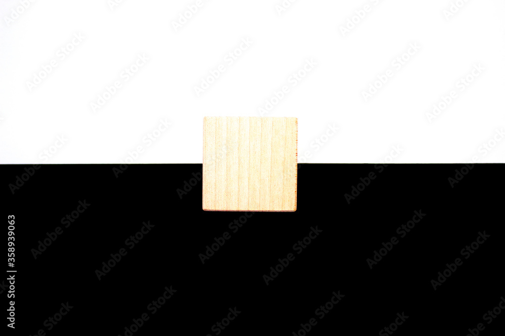 Black and white concept. Two horizontal lines with white on top and black below and a wooden cube in the middle. Abstract background. Balance of duality. Black and white concept. Two horizontal lines with white on top and black below and a wooden cube in the middle. Abstract background. Balance of duality.
