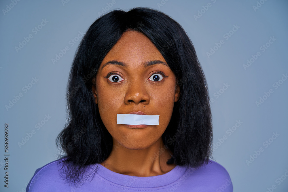 Close-up terrified female face with sealed mouth by white stripe. Emotions concept Close-up terrified female face with sealed mouth by white stripe. Emotions concept