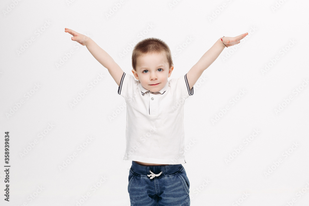 Funny little boy with blue eyes, wearing in white polo t-shirt, jeans, gesturing by hands and showing wings like flying bird, in different sides. Kid playing at studio and enjoying. White background. Funny little boy with blue eyes, wearing in white polo t-shirt, jeans, gesturing by hands and showing wings like flying bird, in different sides. Kid playing at studio and enjoying. White background.