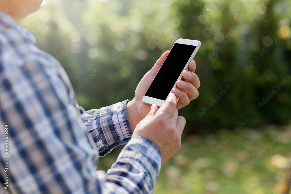 Cropped shot of man hand holding blank screen smartphone blurred nature background.
