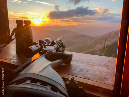 Close up of rifle and binocular for  hunting. View from the window on sunrise. photo
