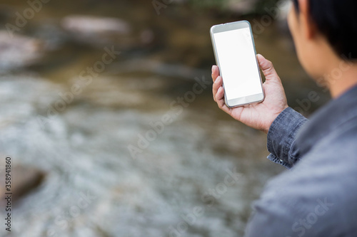 Hand holding smart phone isolated on landscape background of water fall.