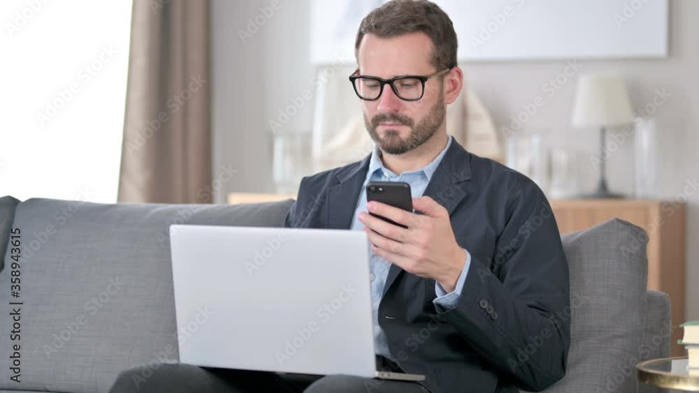 Young Businessman using Smartphone and Laptop at Home 