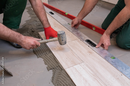 A worker laying ceramic tiles in the bathroom with a rubber mallet gently aligns the floor plane.