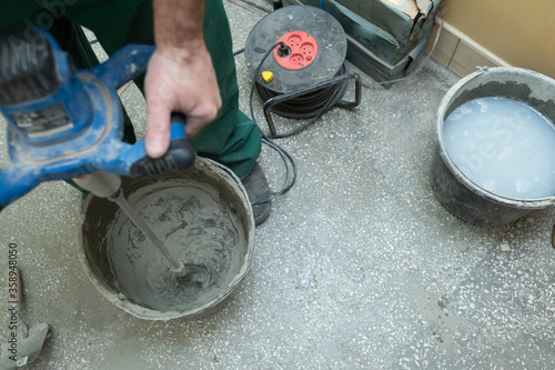 Fotografie A construction worker mixes an adhesive mortar in a black bucket with an electric device
