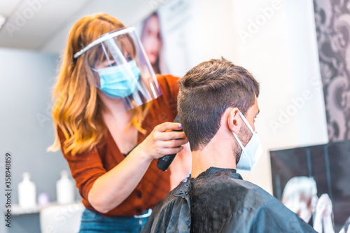 Opening of hairdressing salons after the coronavirus pandemic, covid-19. Security measures, face mask, protective screen, social distance. Hairdressers working on the new normal