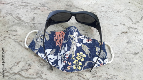 Mask made of cloth And black sunglasses With anti-virus (Covid-19) placed on an outdoor stone table.